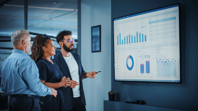 three business professionals analyzing charts on a large screen